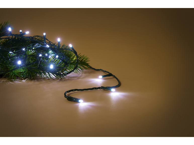 Бели LED коледни лампички върху зелен боров клон, на топъл кафяв фон.