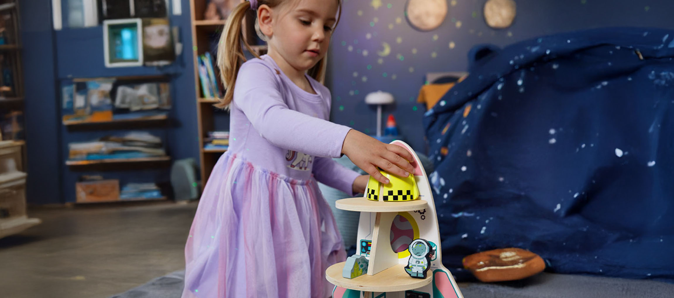 Малко момиче си играе с играчка космически кораб в стая с космическа тема.
