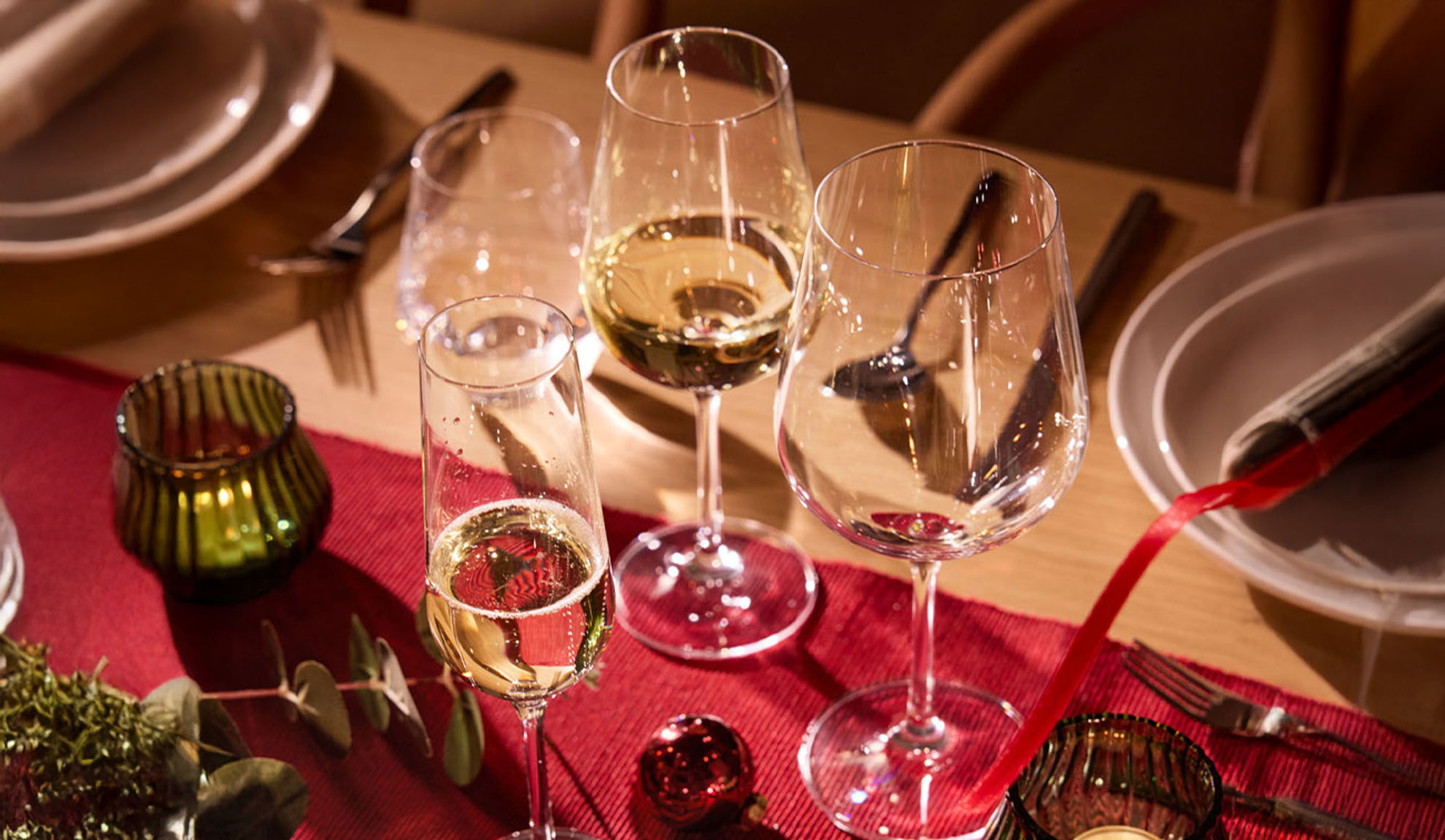 Празнично подредена маса с чаши за вино, чаша за шампанско и коледна украса.