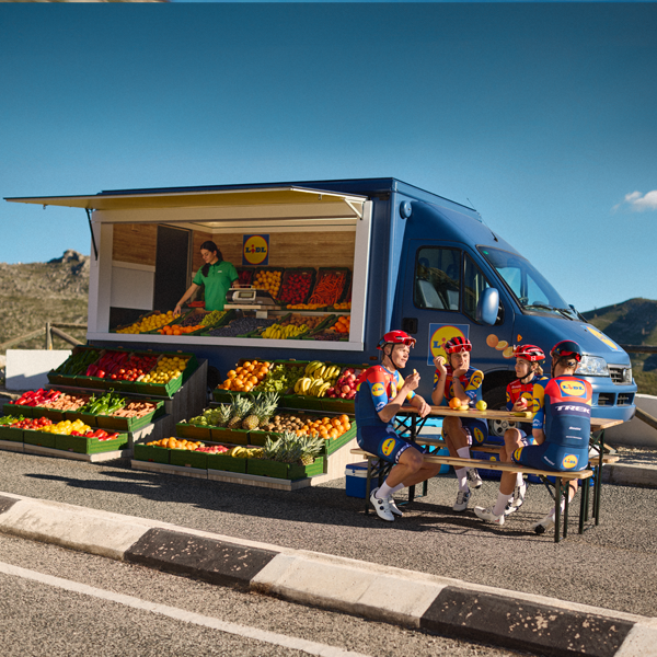Велосипедисти си почиват до камион на Lidl, пълен с плодове и зеленчуци.