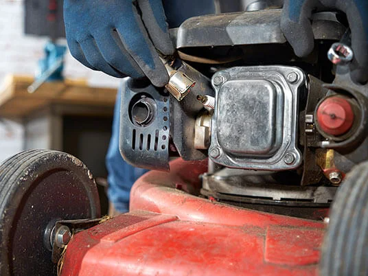 Ръце с ръкавици сменят свещта на червена косачка.