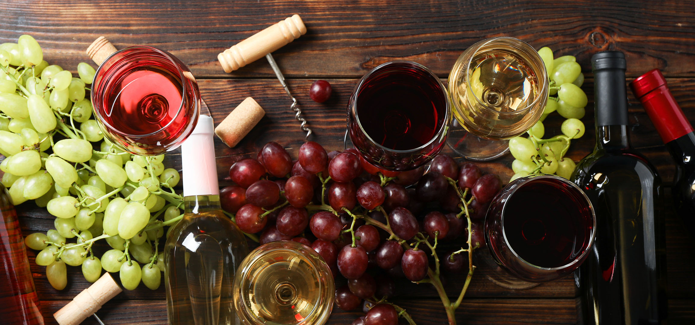 Различни вина, грозде и аксесоари за вино на дървена маса.