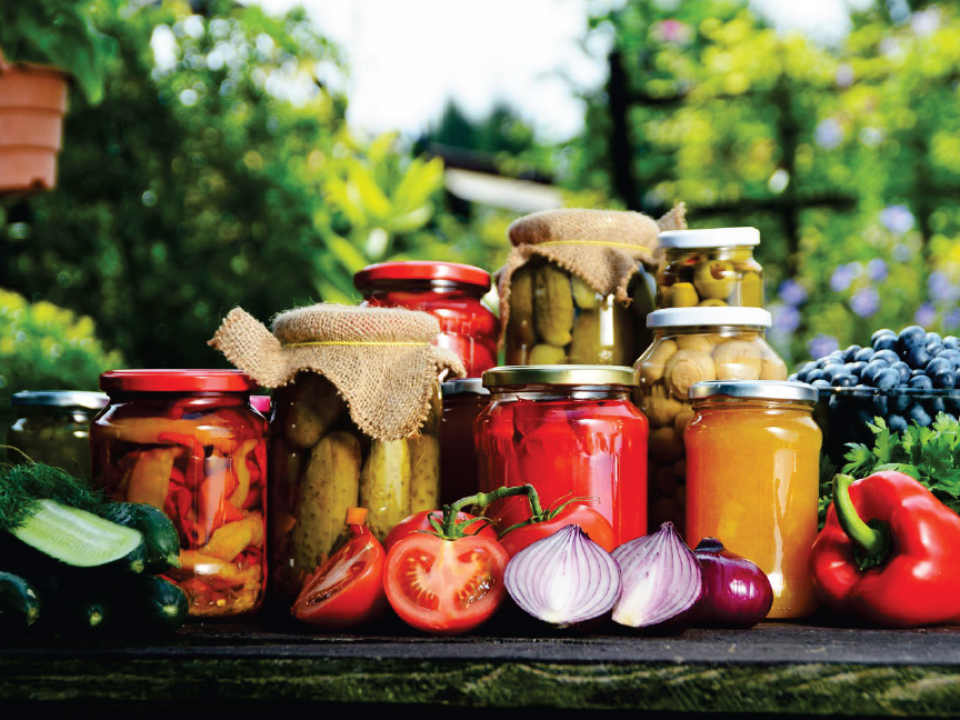 Различни консервирани зеленчуци и пресни продукти на маса на открито.