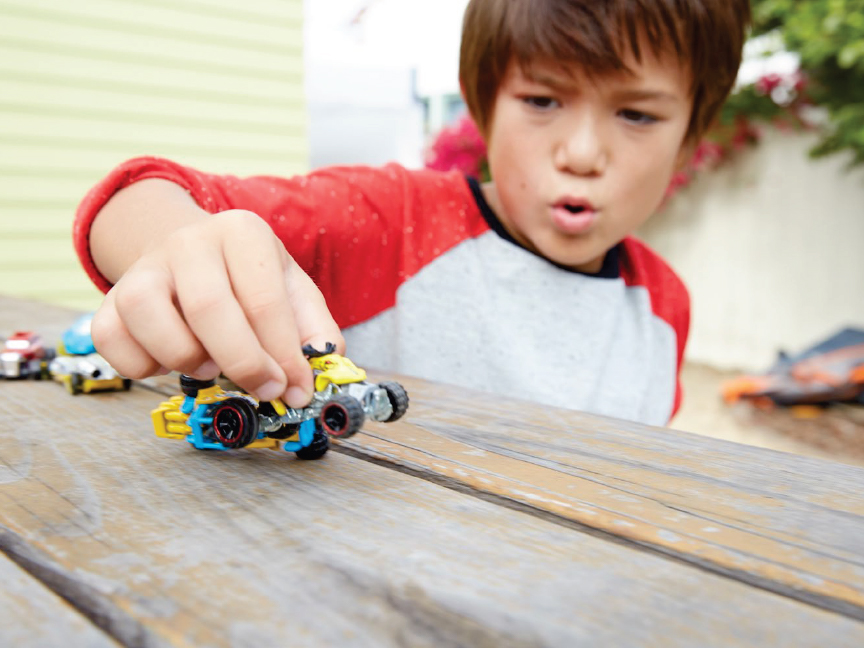 Момче си играе с колички Hot Wheels на маса.