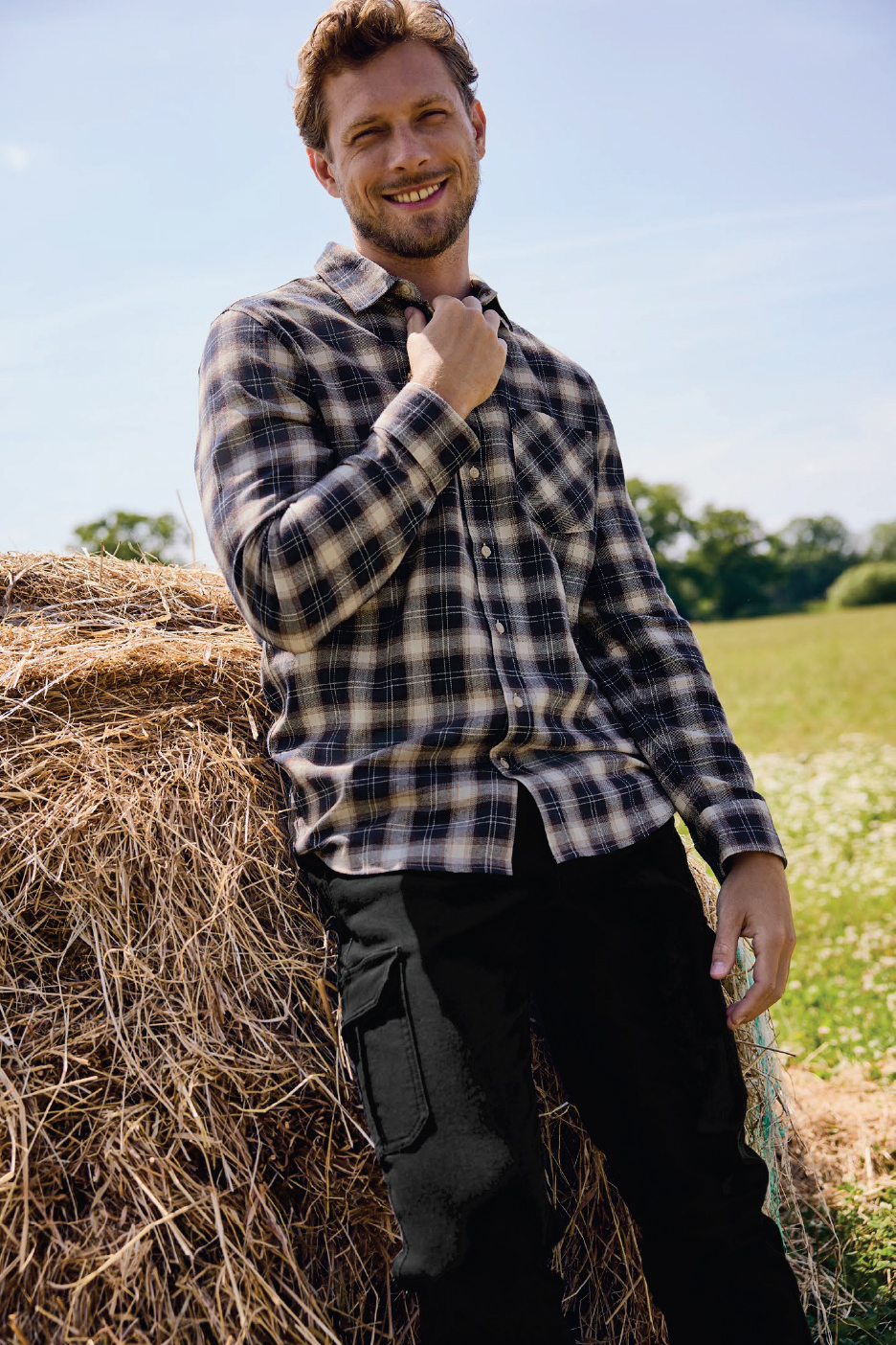Мъж в карирана риза и черни панталони до купа сено