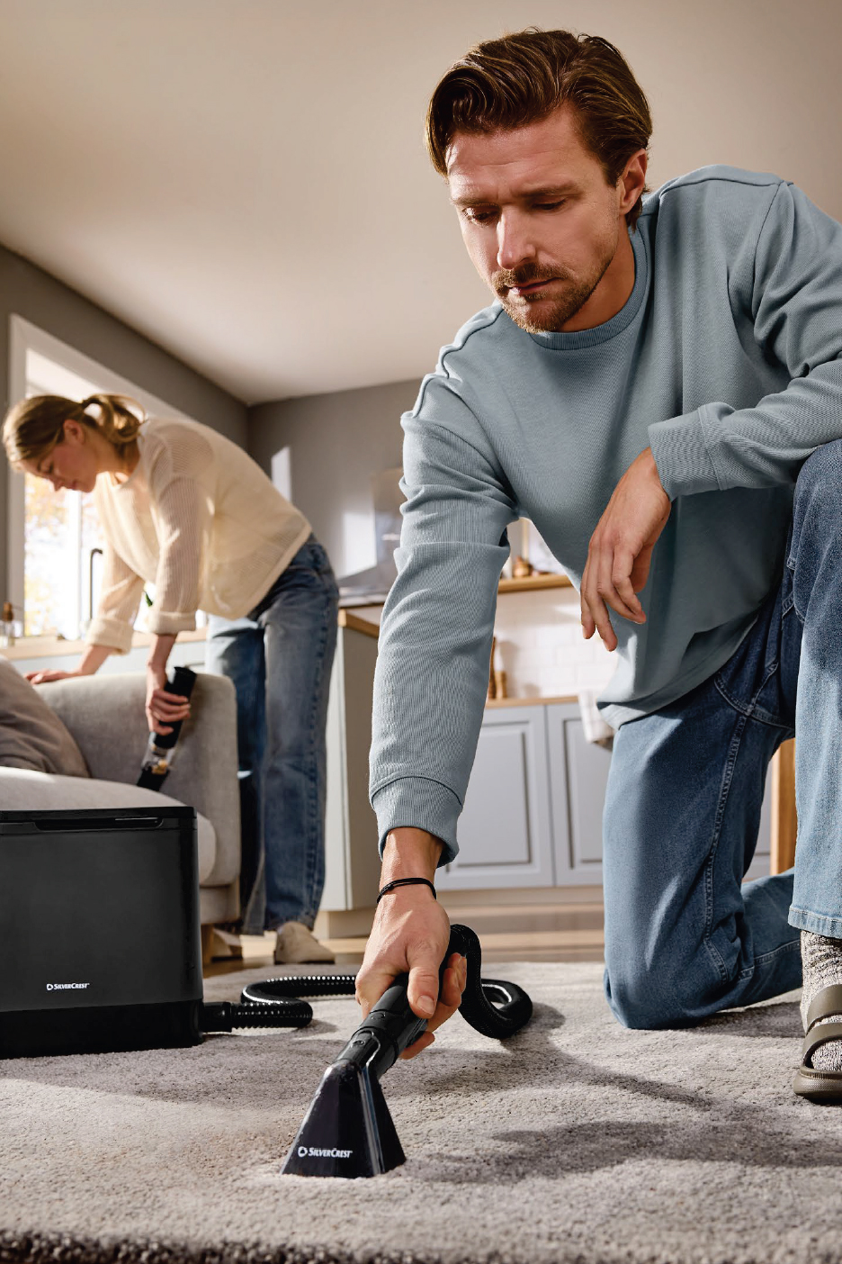 Мъж и жена почистват килим и диван с уреди за почистване на тапицерия.