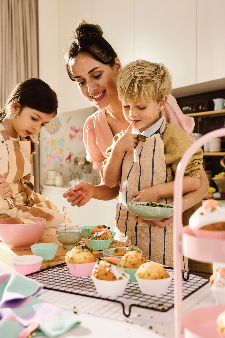 Майка и две деца украсяват мъфини с глазура и поръски в кухнята.