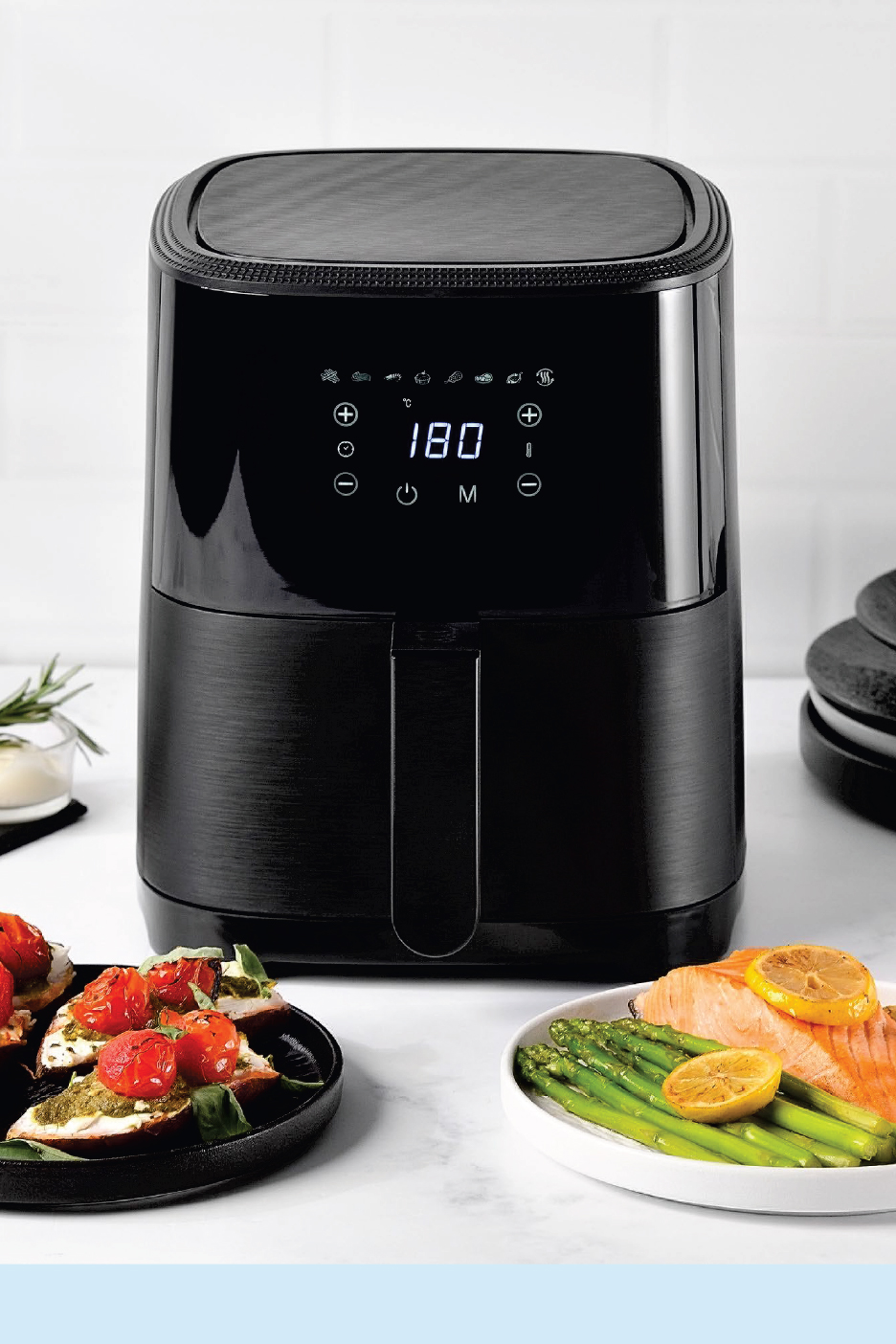 Черен фритюрник с горещ въздух с дигитален дисплей, показващ 180 градуса, до него брускети и сьомга с аспержи.