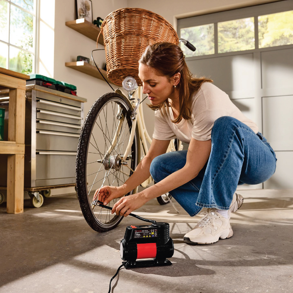 Жена помпа гума на велосипед с електрическа помпа в гараж.