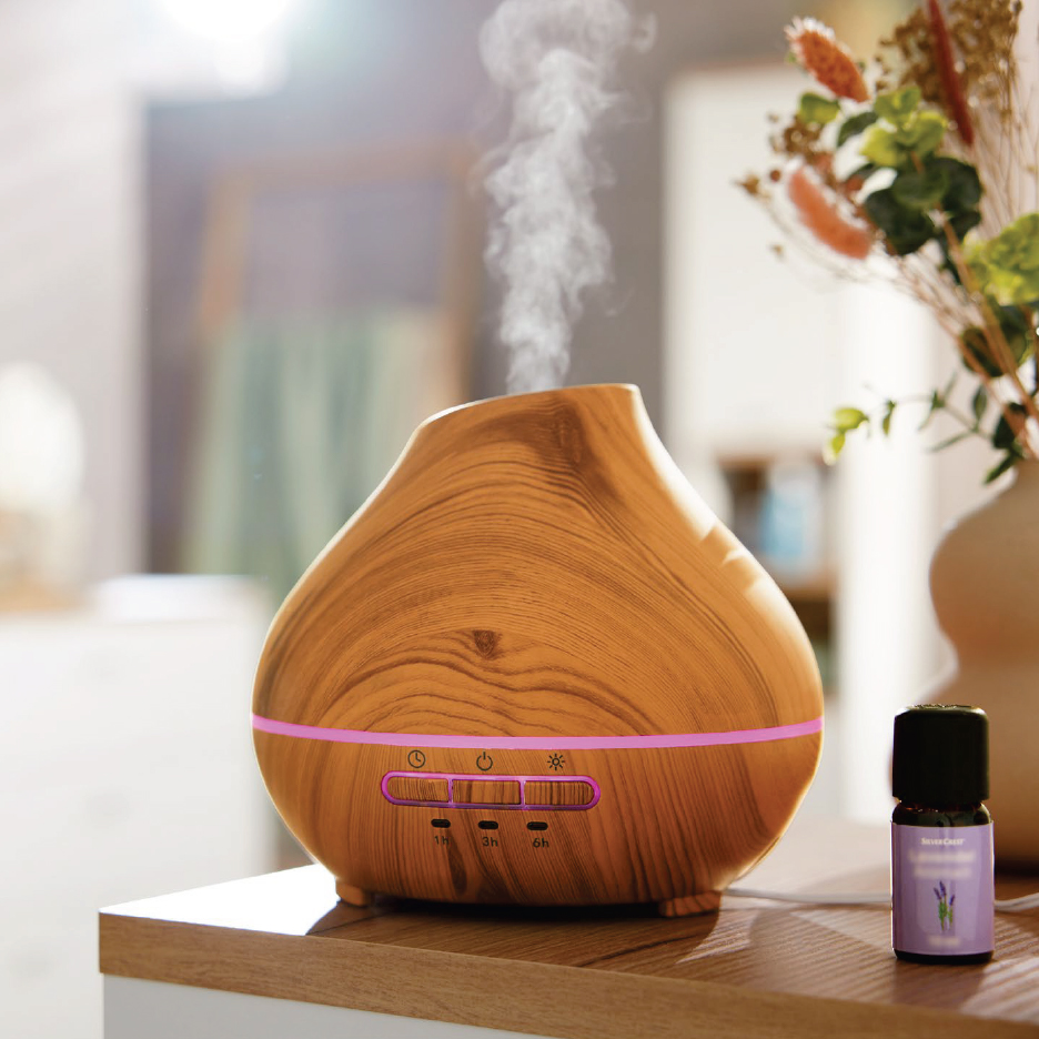 Дървен дифузер за етерични масла с пара и бутилка лавандулово масло на дървен плот.