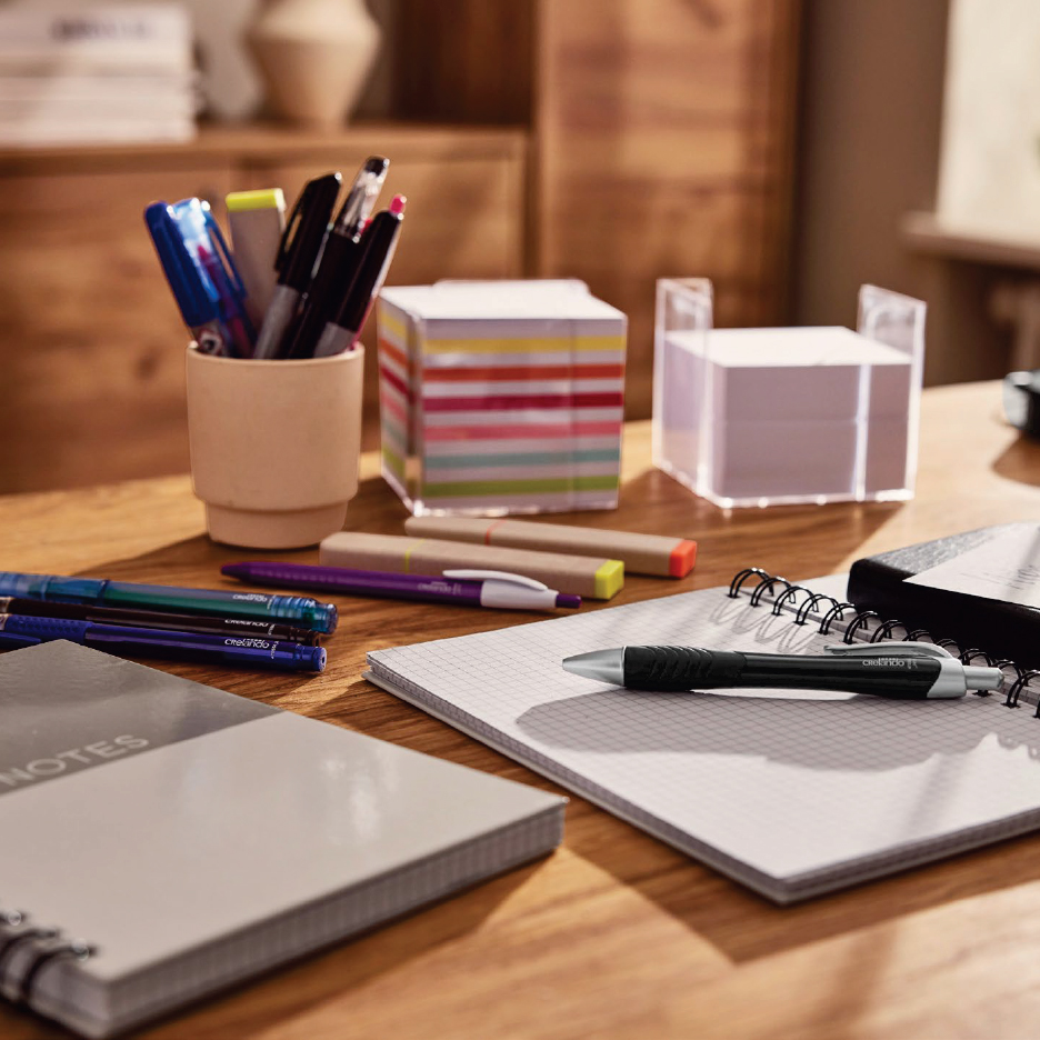 Офис консумативи: тетрадки, химикалки, маркери и блокчета за бележки на дървена маса.