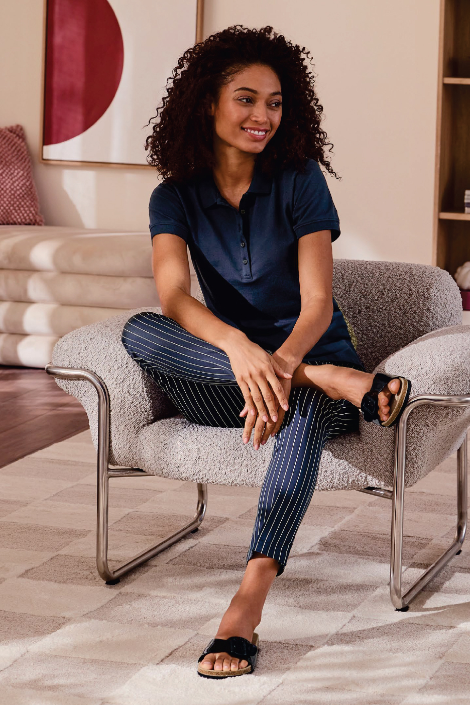 Жена в тъмносиня поло тениска и раиран панталон, седнала на стол.