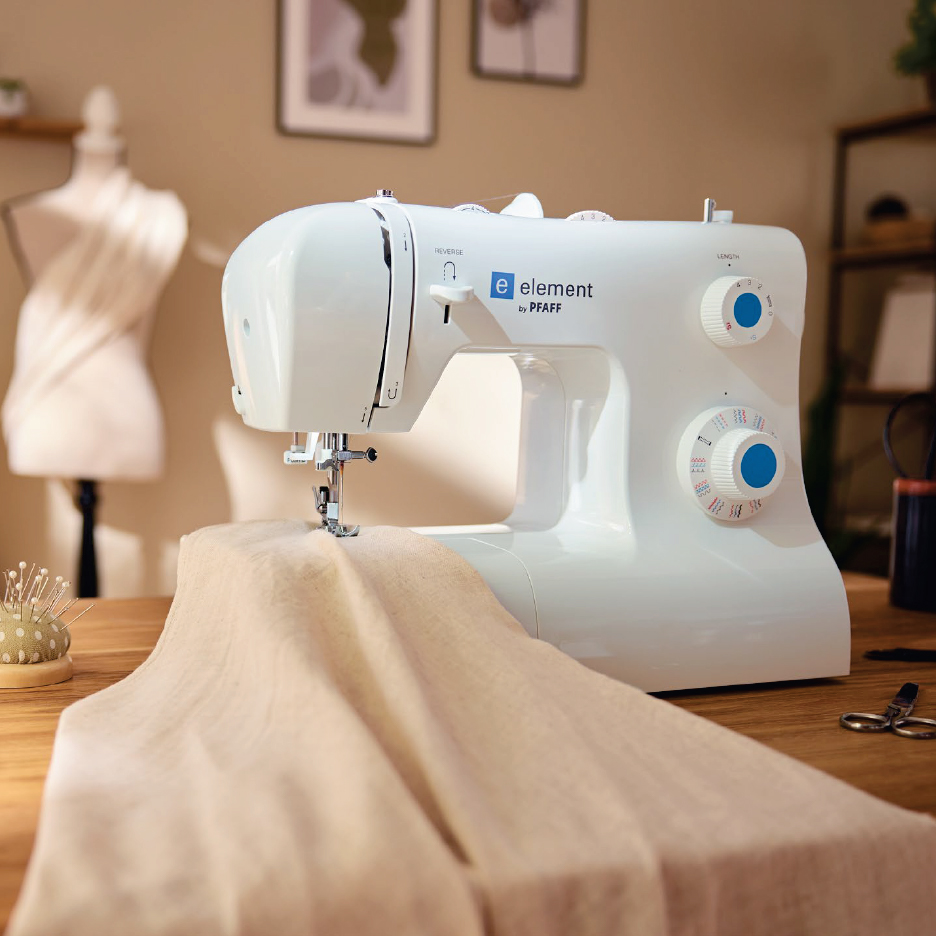 Бяла шевна машина PFAFF Element с плат и аксесоари за шиене на дървена маса.