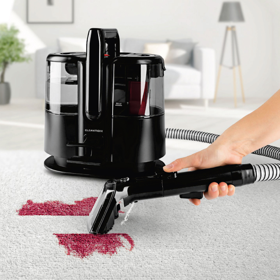 Черен уред за почистване на килими с маркуч и накрайник, почистващ червено петно на бял килим.