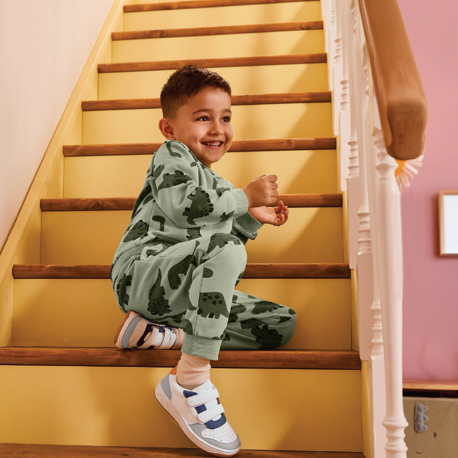 Момче в зелен комплект с динозаври, седнало на стълби