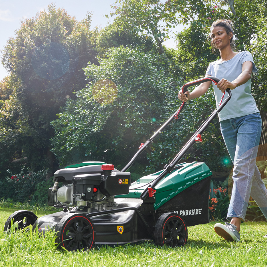 Жена коси трева с косачка Parkside в слънчева градина.