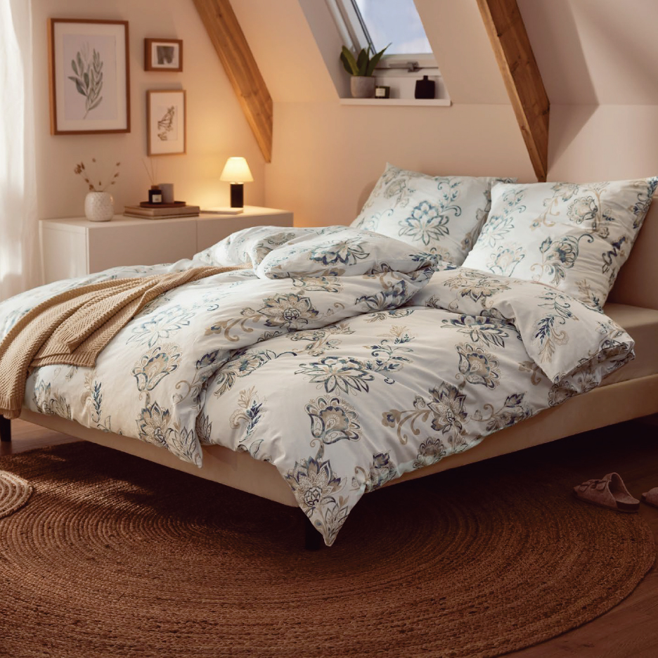 Спалня с легло, завивки с флорални мотиви, нощна лампа и килим от юта.