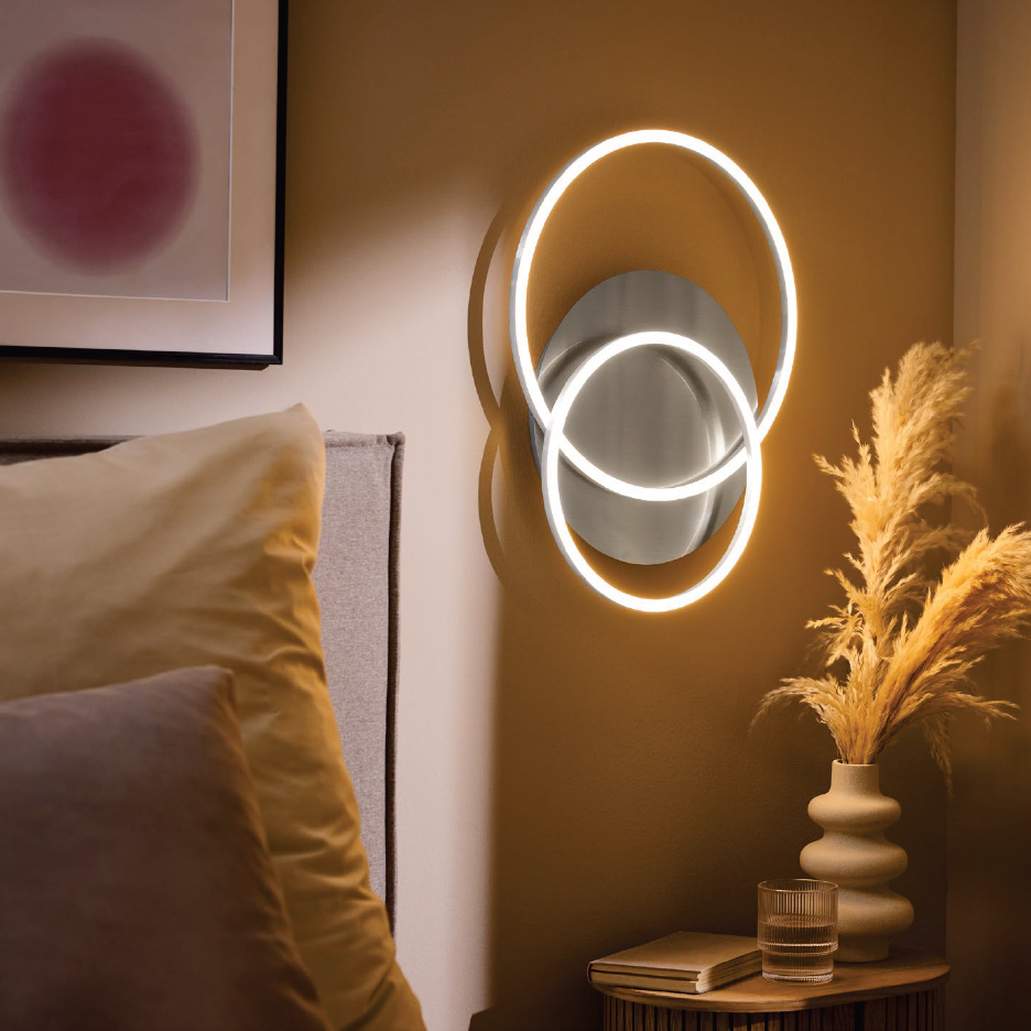 Стенна лампа с LED кръгове над нощно шкафче с ваза и книга до легло