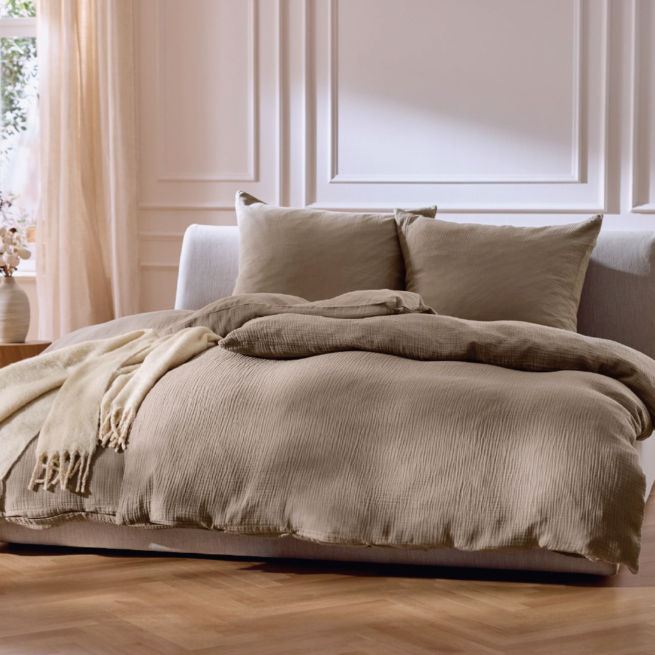 Бежово спално бельо от муселин с две възглавници и одеяло в спалня.