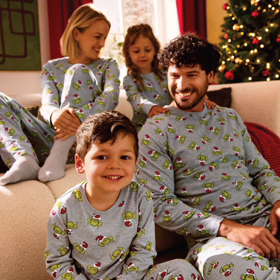 Семейство в еднакви коледни пижами с Гринч, седнало на диван до коледна елха.