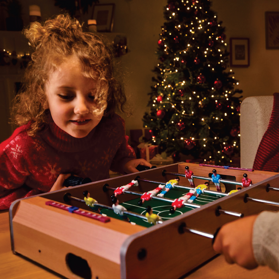 Дете играе футбол на маса пред коледна елха
