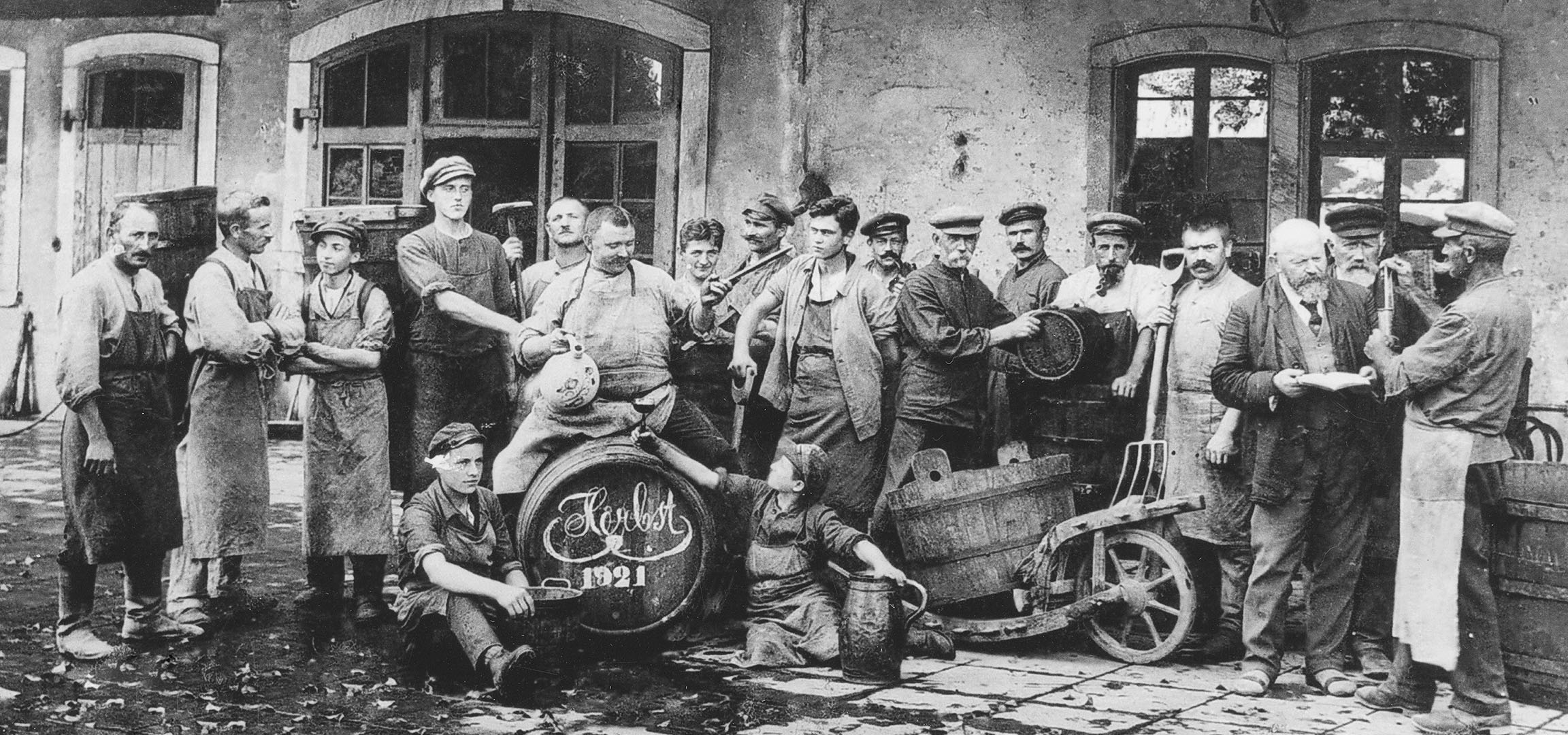Мъже в изба с винени бъчви, един вдига чаша.