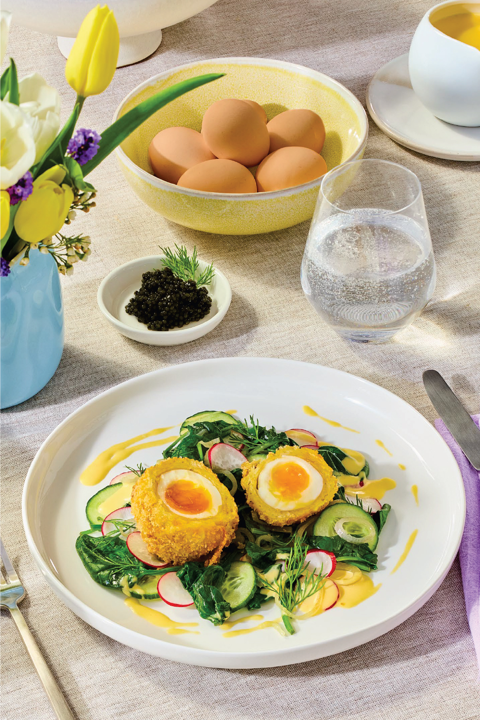 Пържени яйца с течен жълтък, салата, хайвер, яйца и чаша вода на маса.