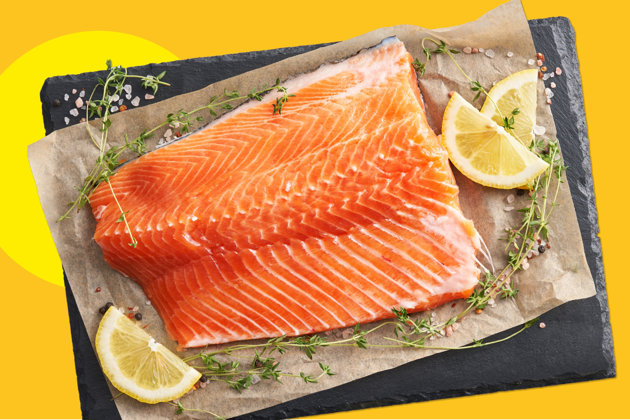 Парче сурова сьомга с лимон и мащерка върху хартия за печене и черен камък.