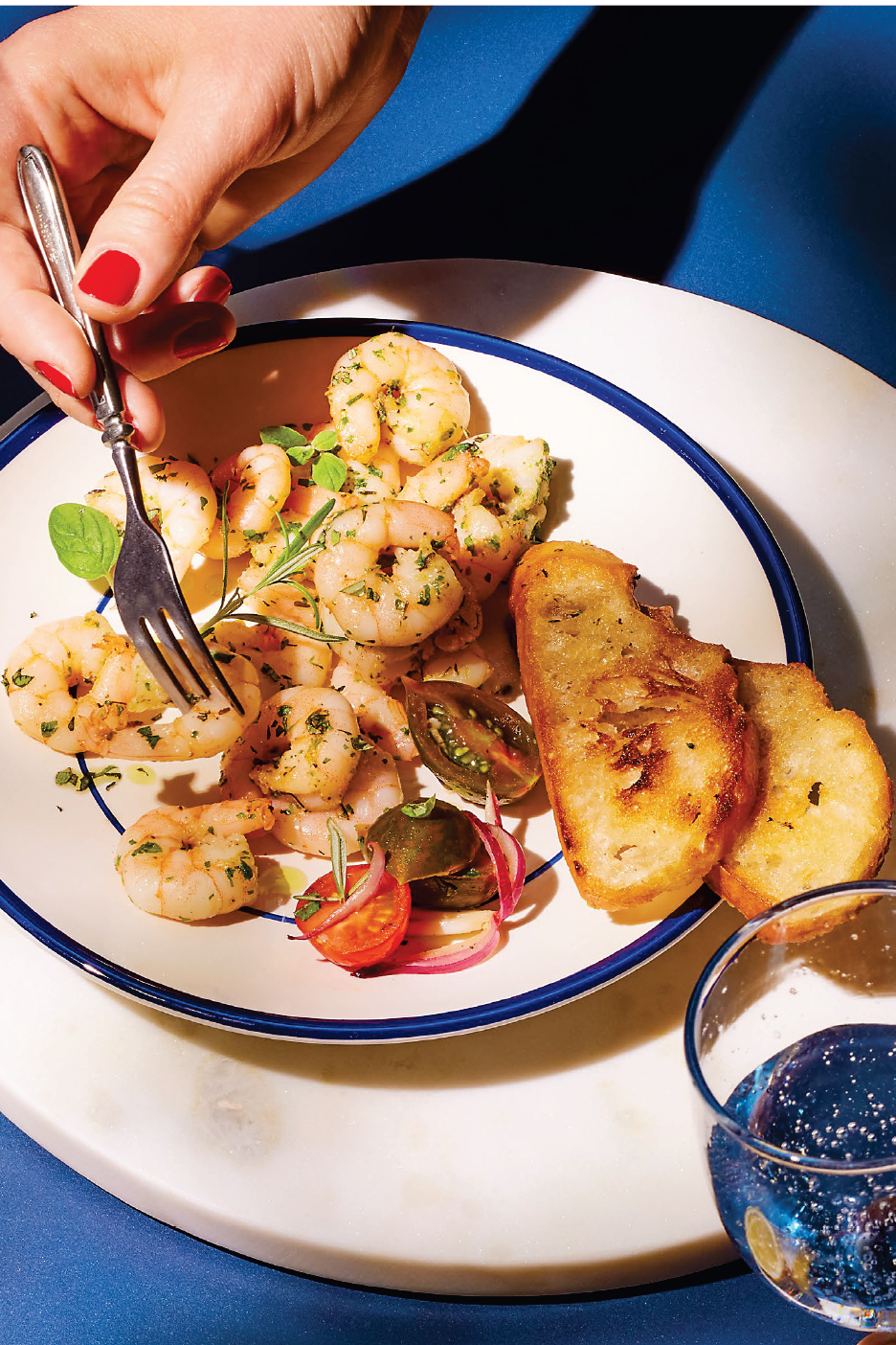 Чиния с приготвени скариди, гарнирани с билки, домати и препечен хляб.