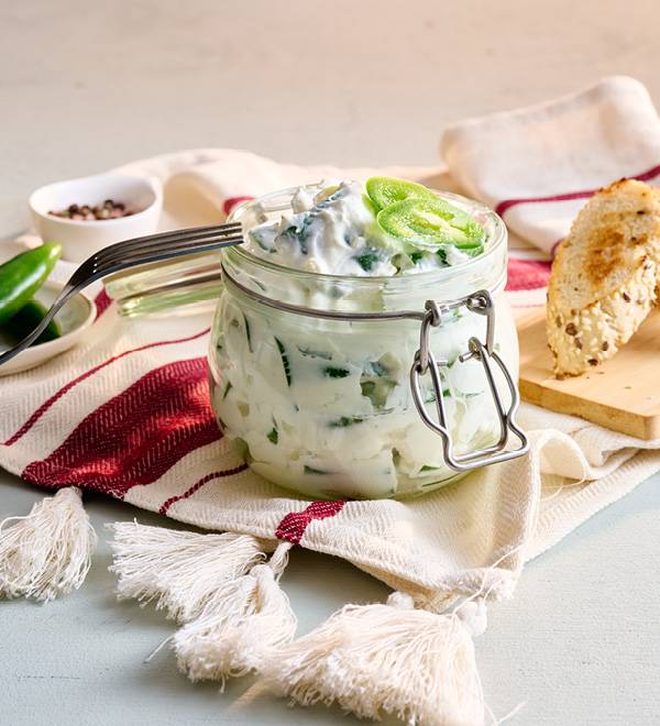 Стъклен буркан с вкусен домашен сос, гарниран с люти чушки, върху бяла текстилна подложка.