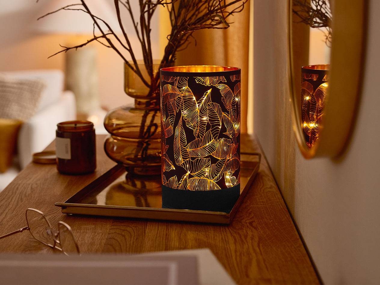 Декоративен LED фенер с шарка на листа, ваза с клони и свещ на дървена маса.