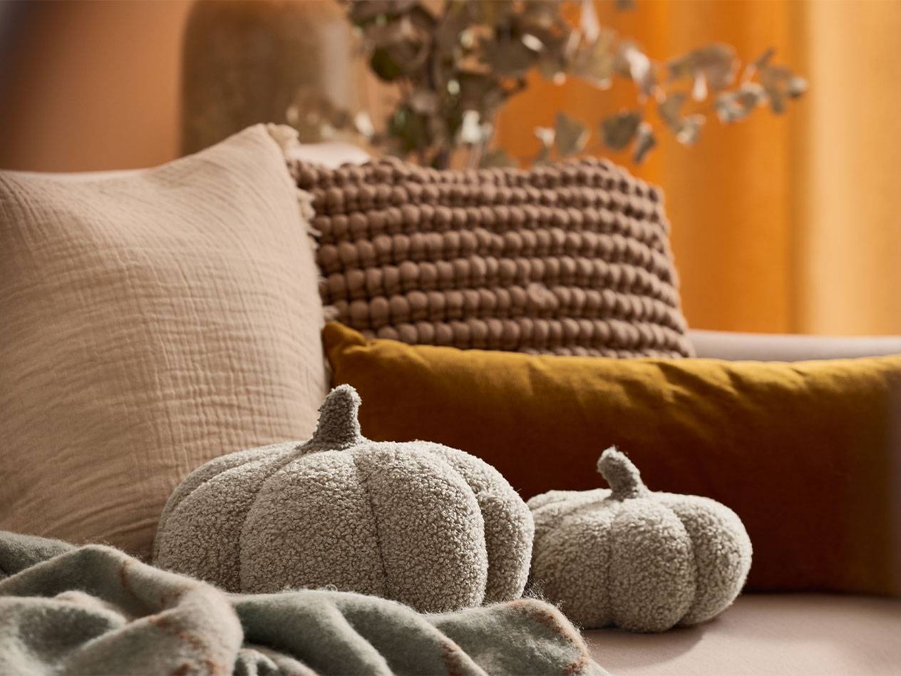 Две плюшени декоративни тикви и възглавници в земни тонове на диван.