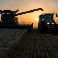 Комбайн и трактор на полето при изгрев.