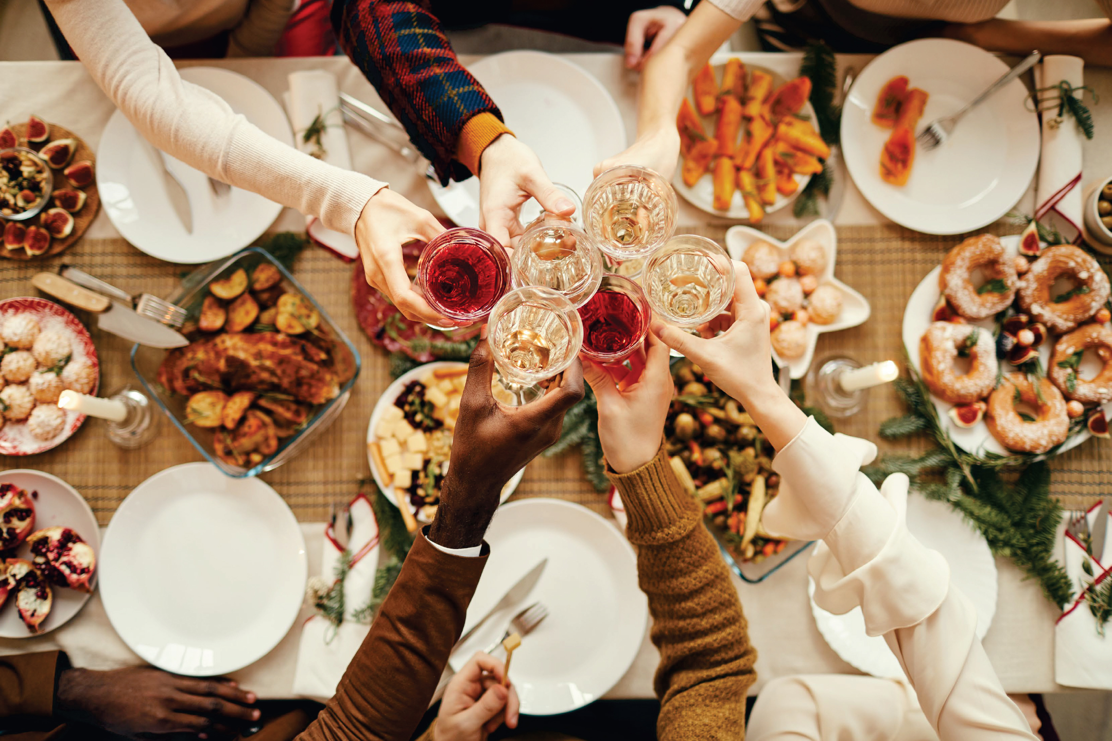 Хора вдигат тост с чаши вино на празнична трапеза с храна.