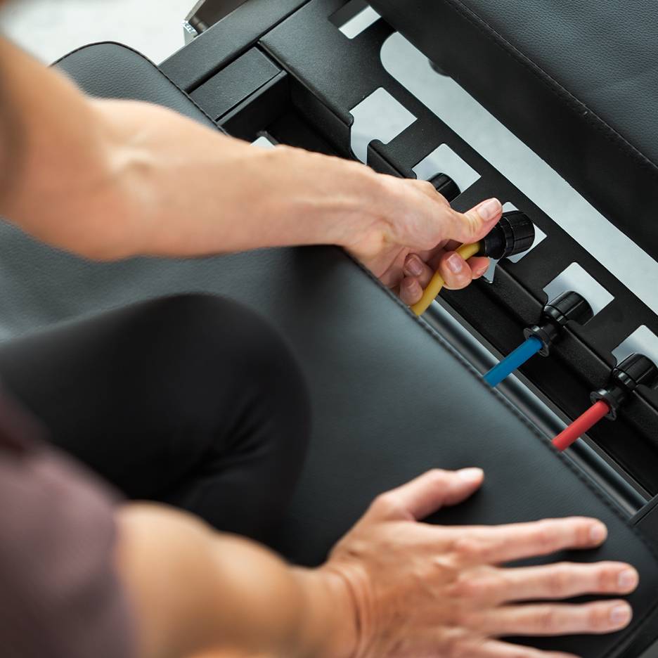 Човек регулира ластици за съпротива на фитнес пейка.