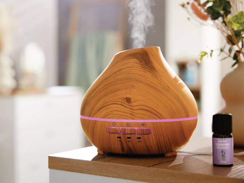 Дървен дифузер за етерични масла с лилава светлина и бутилка лавандулово масло.