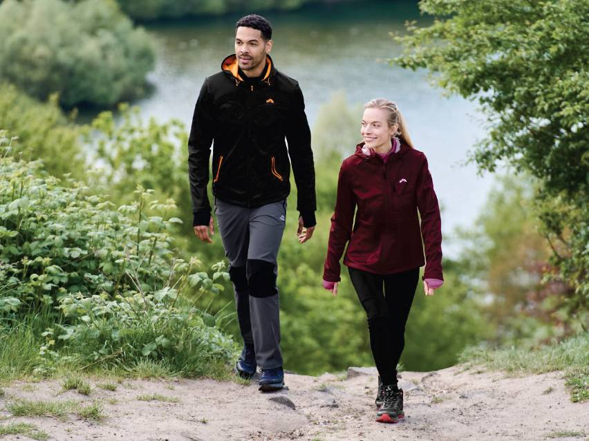 Мъж и жена в спортни якета и панталони вървят по пътека сред природата.