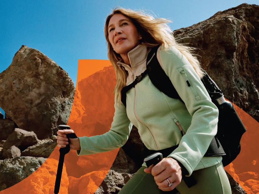 Жена с туристически щеки и раница, облечена в спортно яке и клин, на фона на скалист пейзаж.