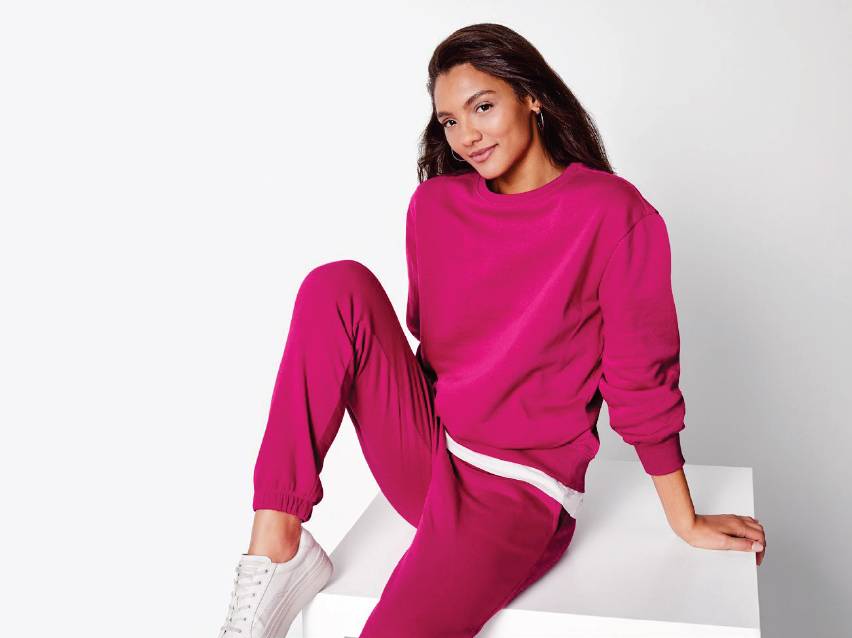 Жена в розова спортна блуза и панталон, седнала на бял куб.