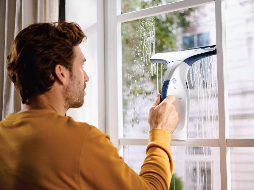 Мъж почиства прозорец с електрическа чистачка за прозорци.