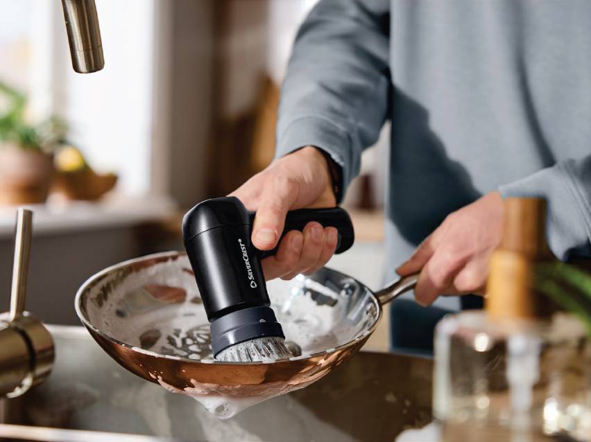 Човек мие тиган с електрическа четка за почистване в кухнята.