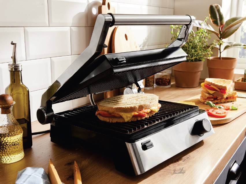 Грил преса с топъл сандвич на дървен плот в кухня.