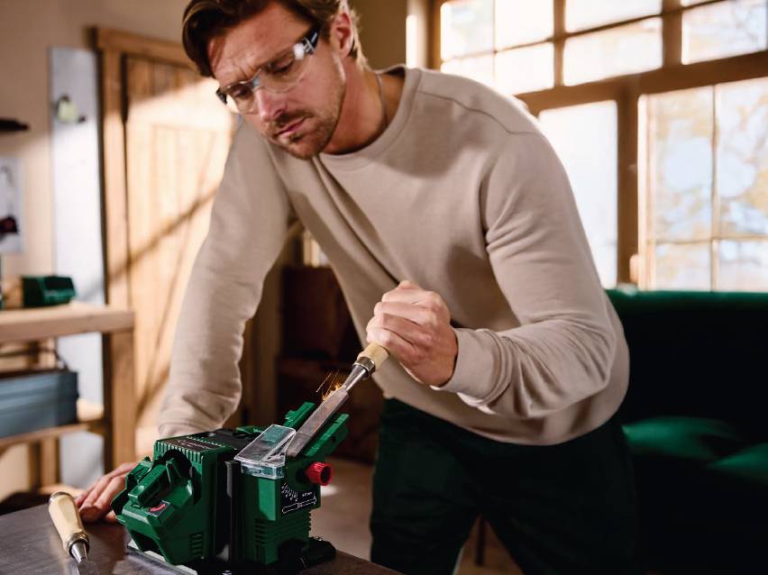 Мъж заточва длето с електрически уред за заточване на инструменти.