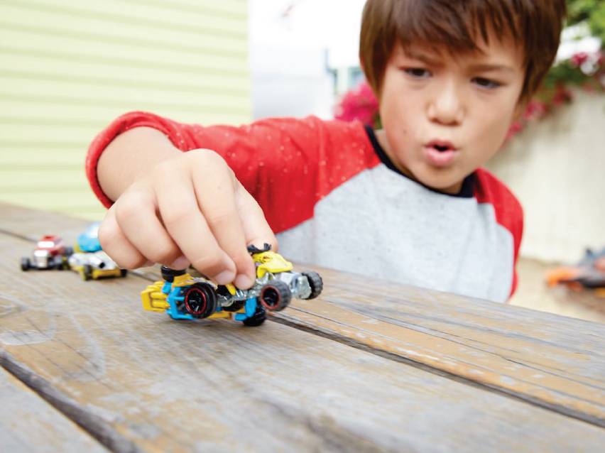 Младо момче си играе с малки играчки колички Hot Wheels на дървена маса.