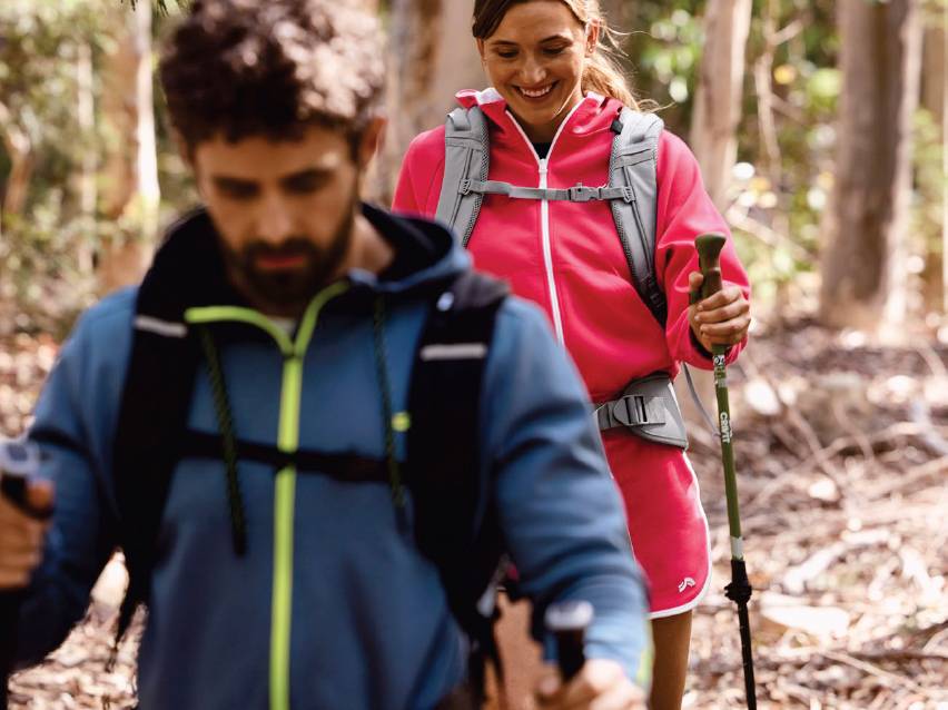 Двама туристи с раници и щеки за трекинг се разхождат в гората.