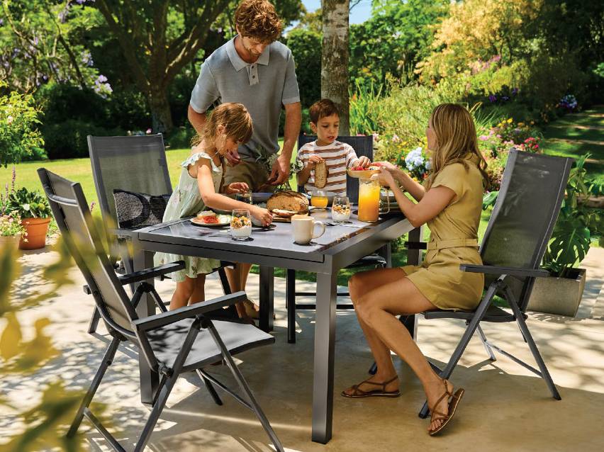 Семейство се храни на открито на сива градинска маса с четири стола.