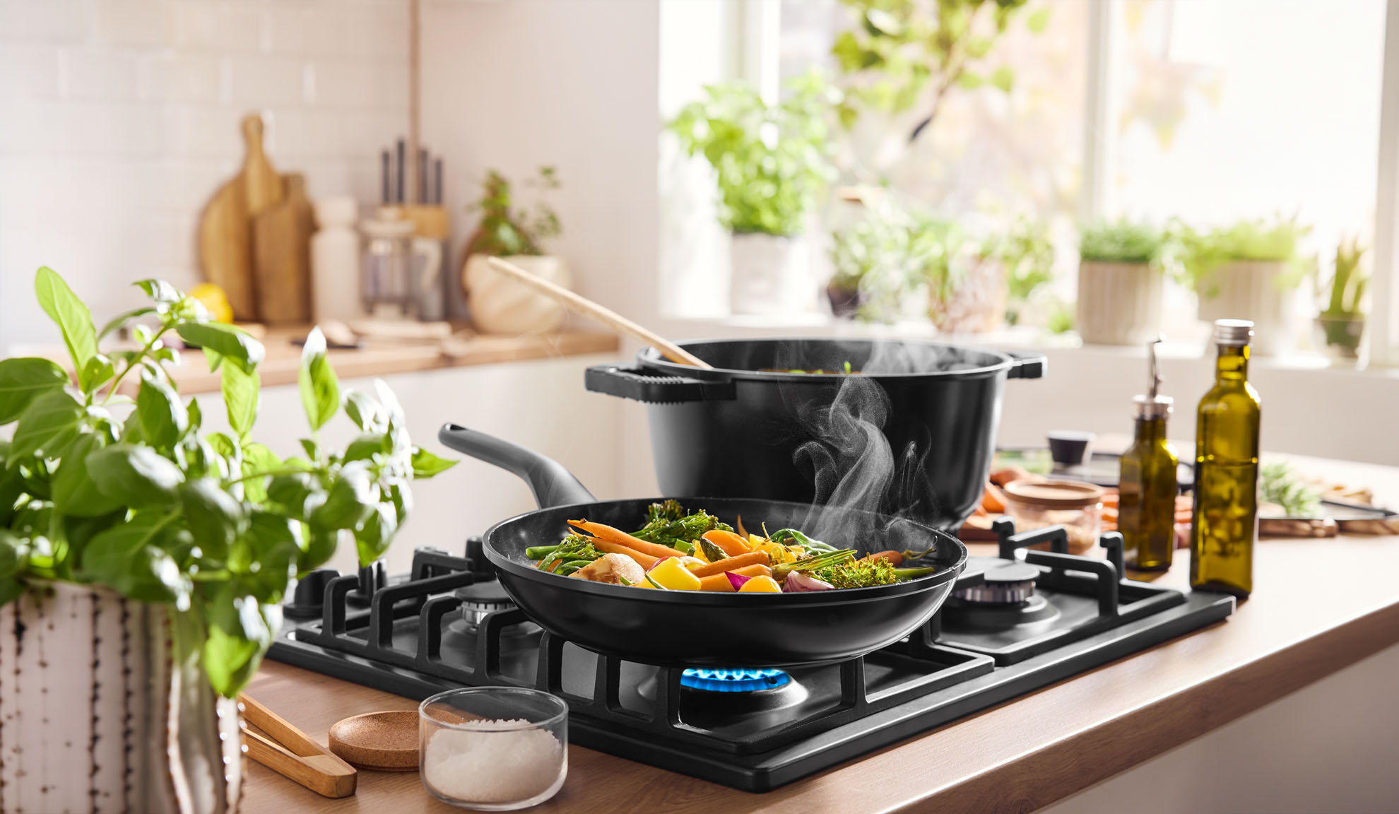 Парещи зеленчуци, готвещи се в тиган и тенджера на газов котлон в светла кухня.