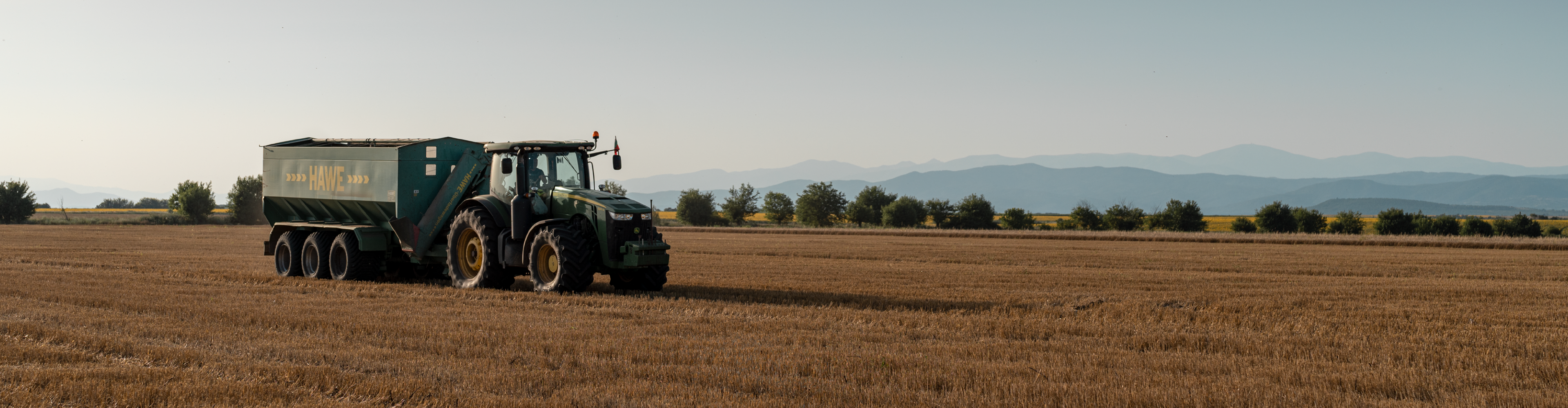Трактор John Deere с прикачен HAWE ремарке в поле.