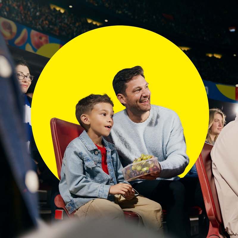 Баща и син се наслаждават на плодове в кутия по време на спортно събитие.