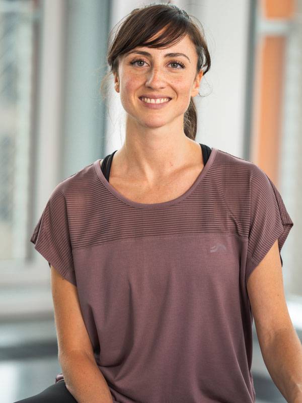 Усмихната жена, облечена в лилав спортен топ с къс ръкав.